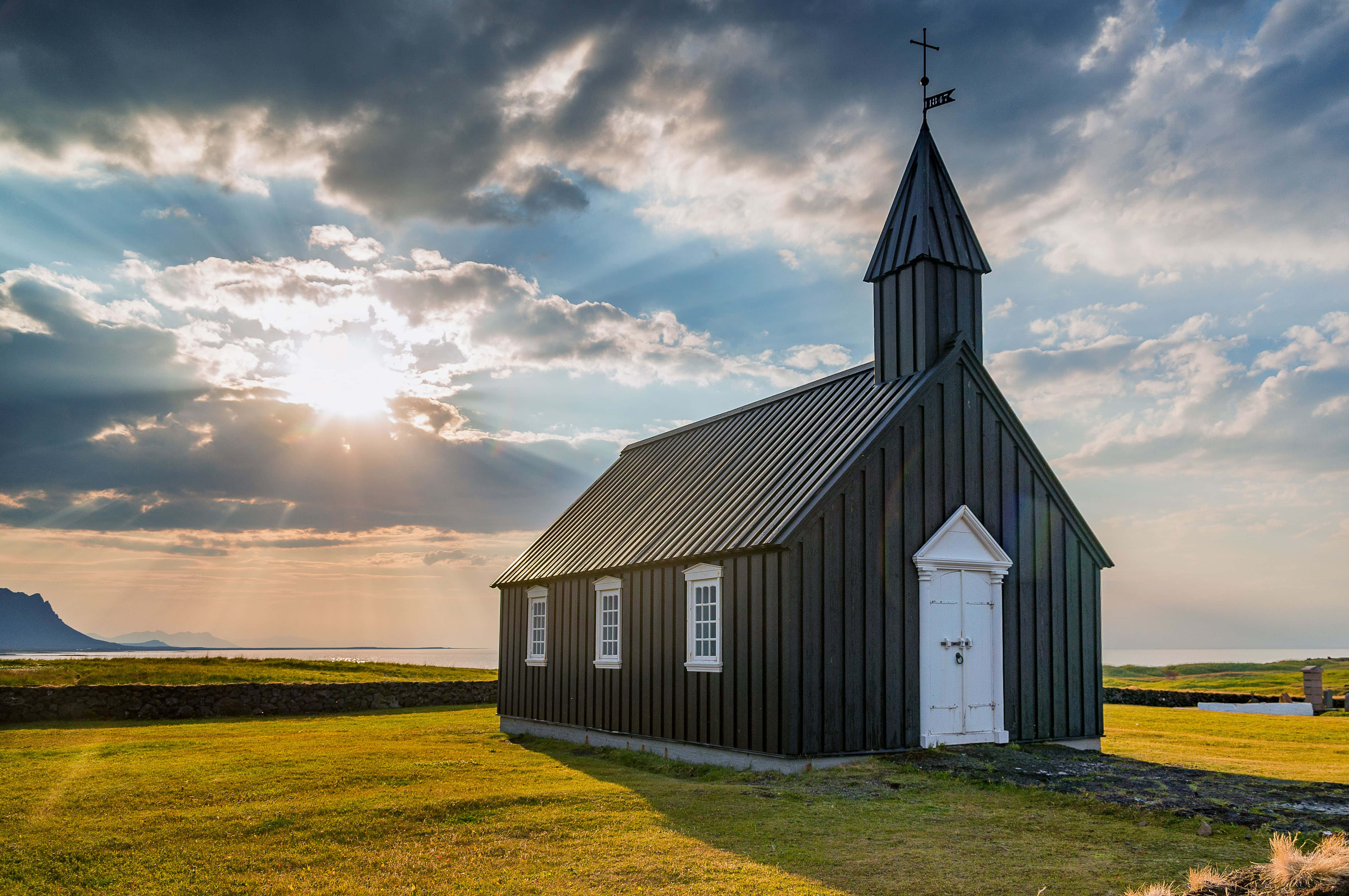 a black church sits on a grassy field Picha ya Ukuta