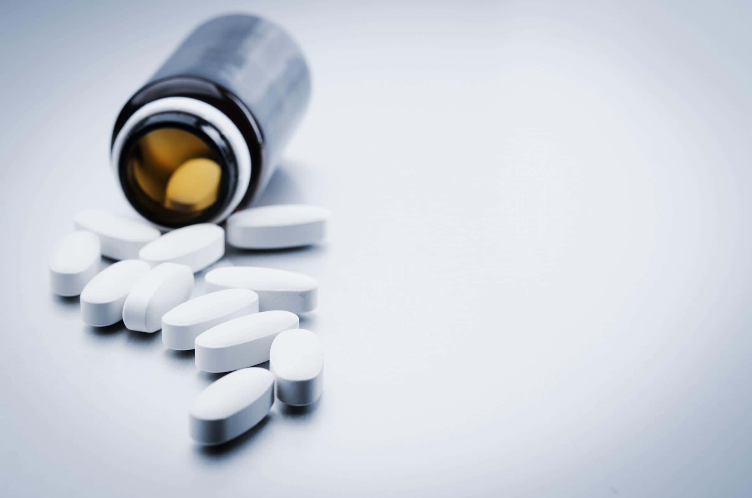 a bottle of pills spilling out onto a white surface Picha ya Ukuta