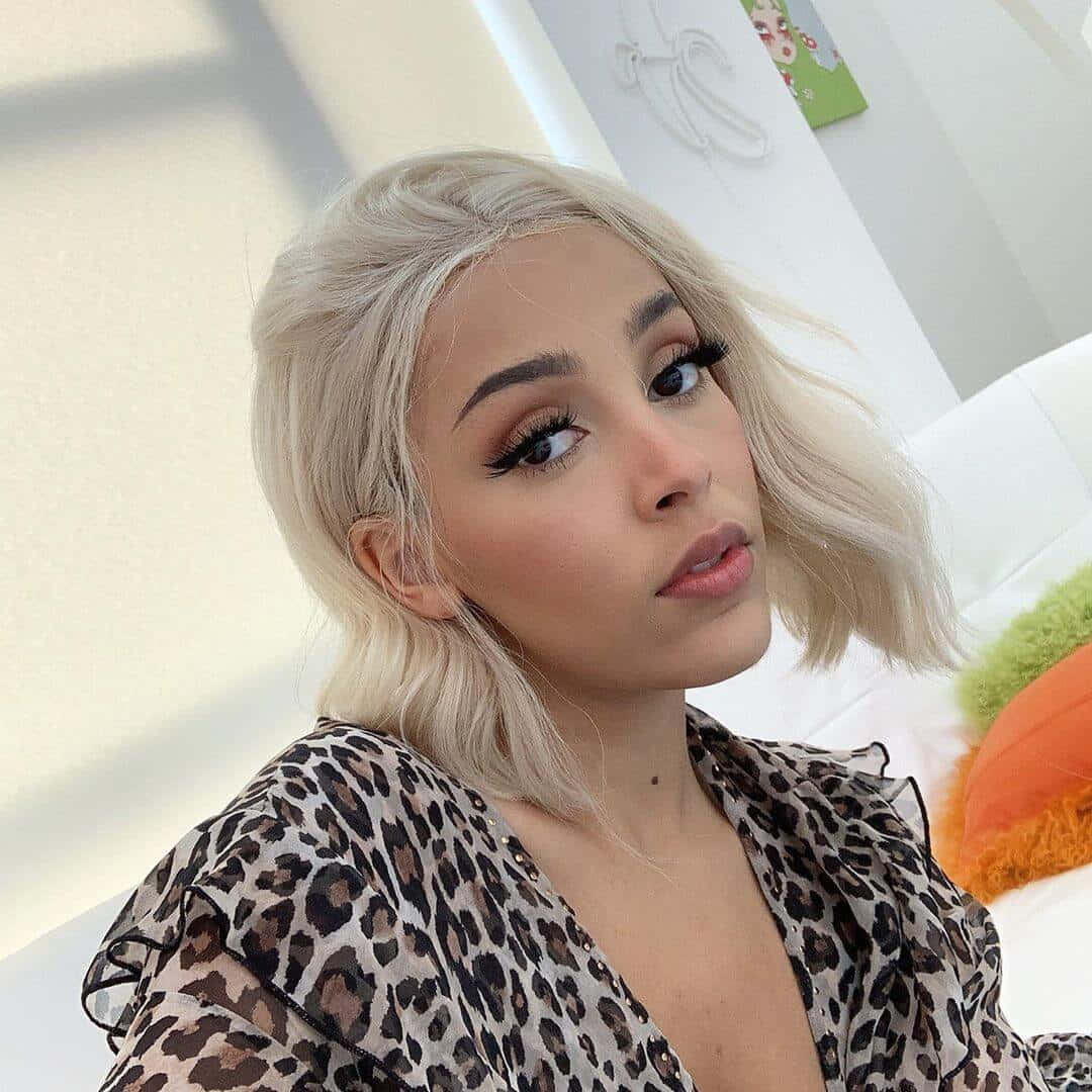 Doja Cat akionyesha uzuri wake katika kivuli cha macho chenye kung'aa na tabasamu angavu. Picha ya Ukuta
