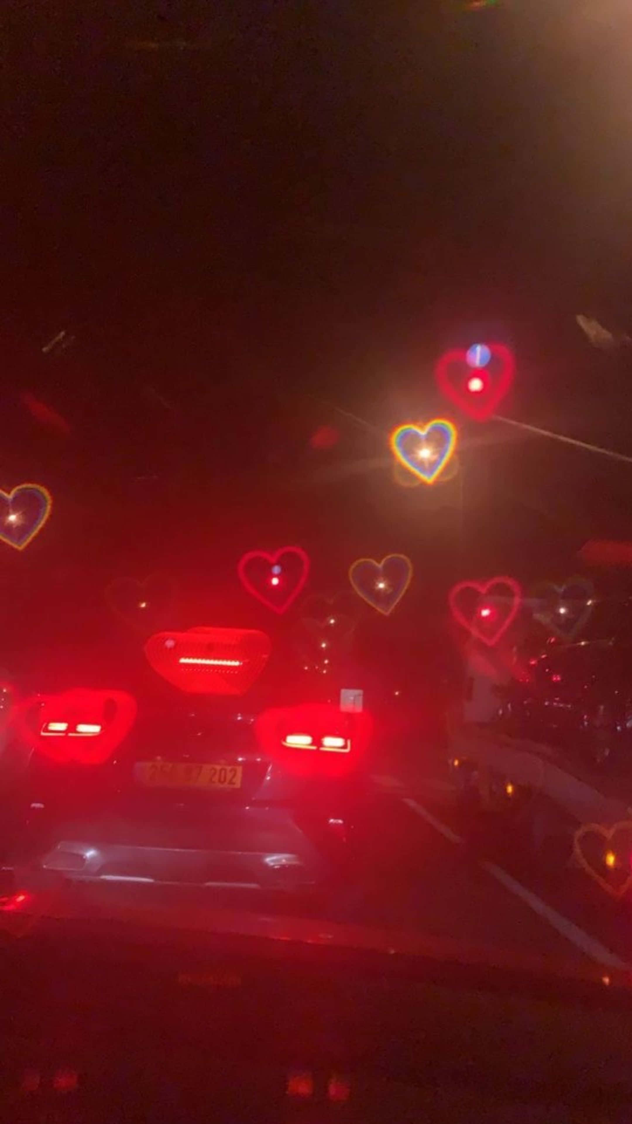 Gari likiendesha barabarani usiku kukiwa na mioyo kwenye kioo cha mbele Picha ya Ukuta