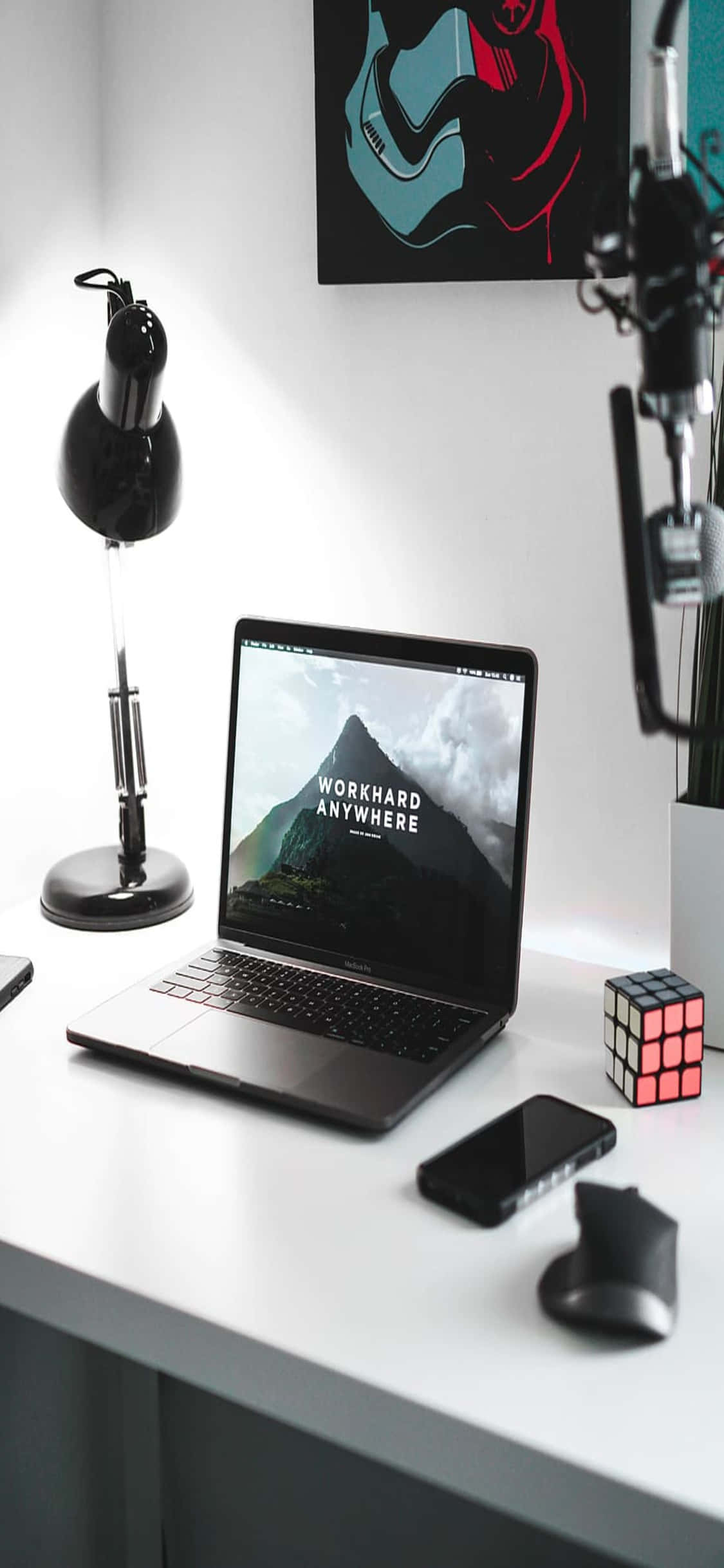 a desk with a laptop, phone, and a lamp Picha ya Ukuta