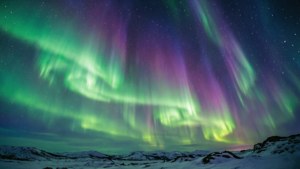 Aurora boreali yenye kung'aa yenye mawimbi ya kijani na zambarau juu ya mandhari yenye theluji. — Mtazamo wa anga Picha ya Ukuta