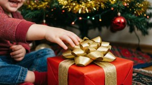 Mkono wa mtoto ukinyosha zawadi nyekundu chini ya mti wa Krismasi.
