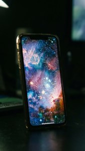 Skrini ya iPhone 17 ikiangaza na mandhari ya galaksi gizani.