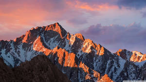 Kilele cha mlima kilichopwa na theluji chini ya machweo wa anga ya rangi ya machungwa wallpaper